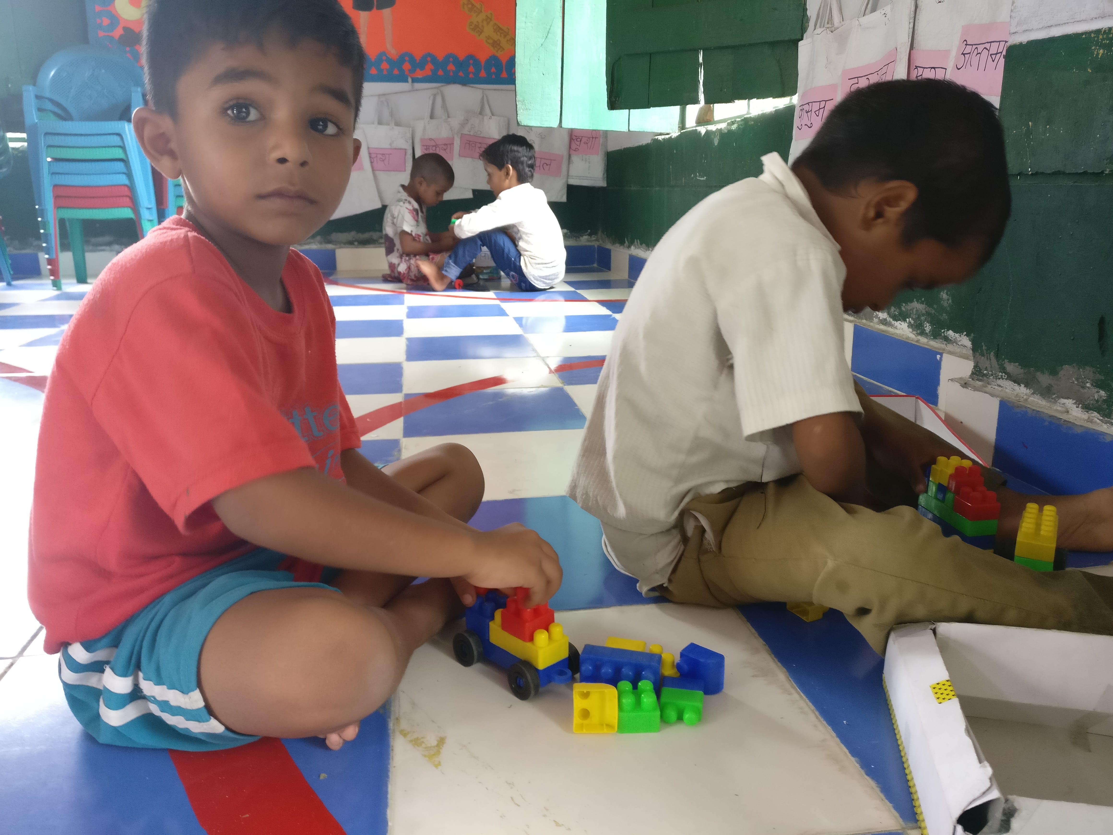 Altamas, 5, and his friend play with building blocks. Play areas are defined with tape. Bags with name tags hanging on the wall were made with the packaging the nutritional supplement came in. Photo credit: Shreya Roy Chowdhury Altamas, 5, and his friend play with building blocks. Play areas are defined with tape. Bags with name tags hanging on the wall were made with the packaging the nutritional supplement came in. Photo credit: Shreya Roy Chowdhury