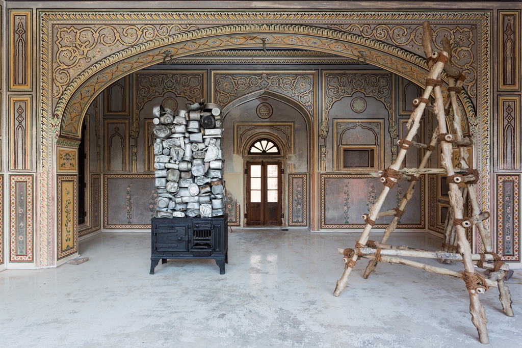 Left–Subodh Gupta, Stove, 2013, Found aluminum utensils and found cast-iron stove. Right – Jitish Kallat, Vertical Chronicle of a Turbulent Equilibrium, 2013, Pigmented resin, steel and rope. Credit: Dhruv Malhotra. Courtesy: Saat Saath Arts Left–Subodh Gupta, Stove, 2013, Found aluminum utensils and found cast-iron stove. Right – Jitish Kallat, Vertical Chronicle of a Turbulent Equilibrium, 2013, Pigmented resin, steel and rope. Credit: Dhruv Malhotra. Courtesy: Saat Saath Arts