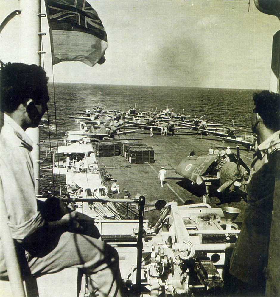 Two young members of the squadron, looking at their aircraft on the carrier deck. The nearest aircraft (with folded wings) is an American type, possibly one of a number of Lend-Lease aircraft that were disposed of on this voyage by being pushed overboard in the Cochin Channel. Photo Courtesy: Late Wing Commander CHL Digby's family Two young members of the squadron, looking at their aircraft on the carrier deck. The nearest aircraft (with folded wings) is an American type, possibly one of a number of Lend-Lease aircraft that were disposed of on this voyage by being pushed overboard in the Cochin Channel. Photo Courtesy: Late Wing Commander CHL Digby's family