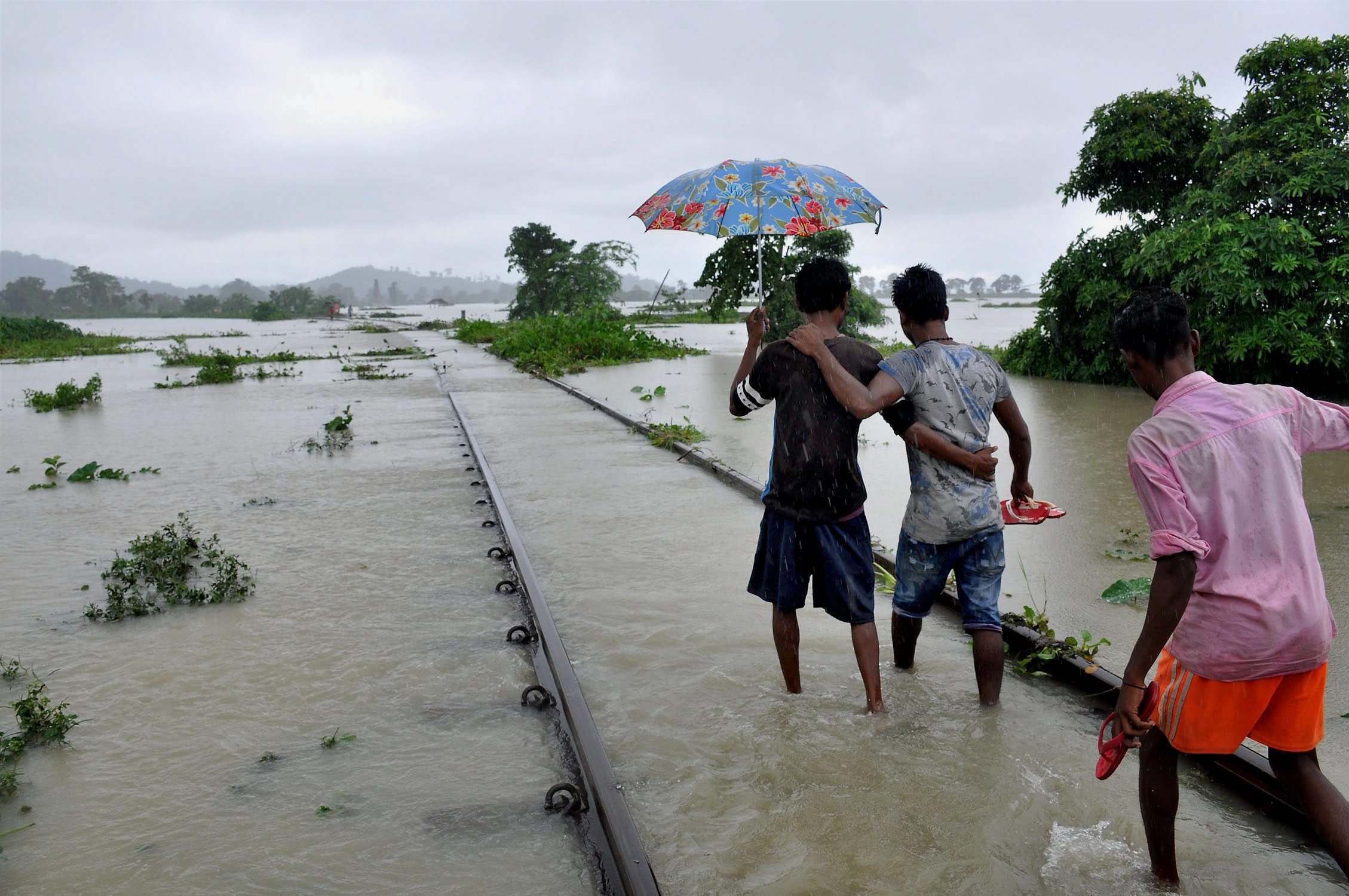 People walk in ankle-deep waters along a submerged railway track in Nagaon district in Assam. (Credit: PTI) People walk in ankle-deep waters along a submerged railway track in Nagaon district in Assam. (Credit: PTI)