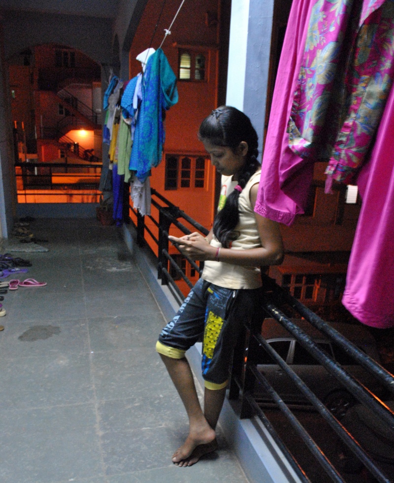 After dinner, a young woman at a garment workers hostel in Bengaluru takes a moment to text her sister in Odisha on WhatsApp. Photo credit: Rohini Mohan. After dinner, a young woman at a garment workers hostel in Bengaluru takes a moment to text her sister in Odisha on WhatsApp. Photo credit: Rohini Mohan.