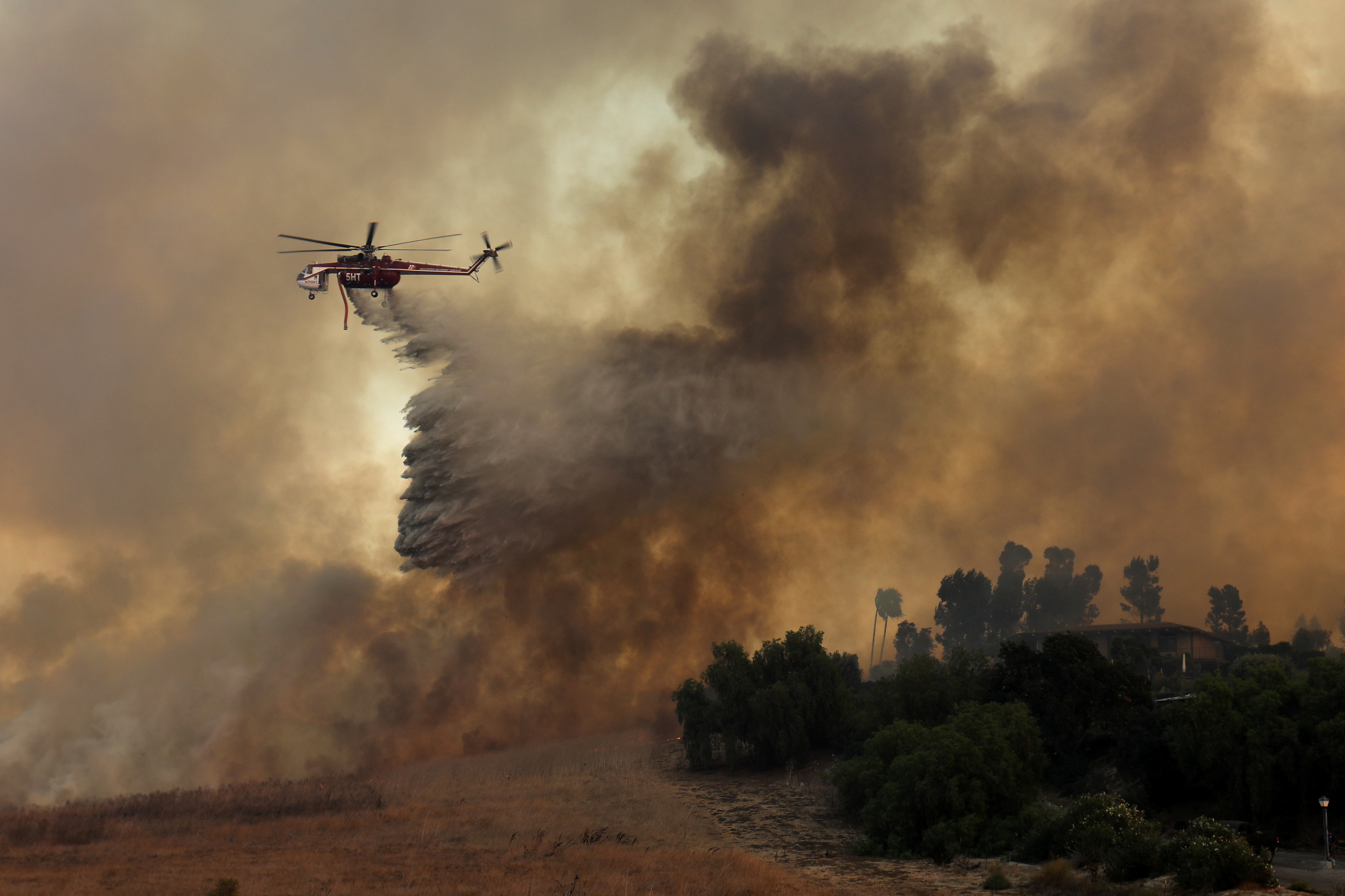 A firefighting helicopter drops water to help save a home during a wildfire. (Photo Credit: Mike Blake/Reuters) A firefighting helicopter drops water to help save a home during a wildfire. (Photo Credit: Mike Blake/Reuters)
