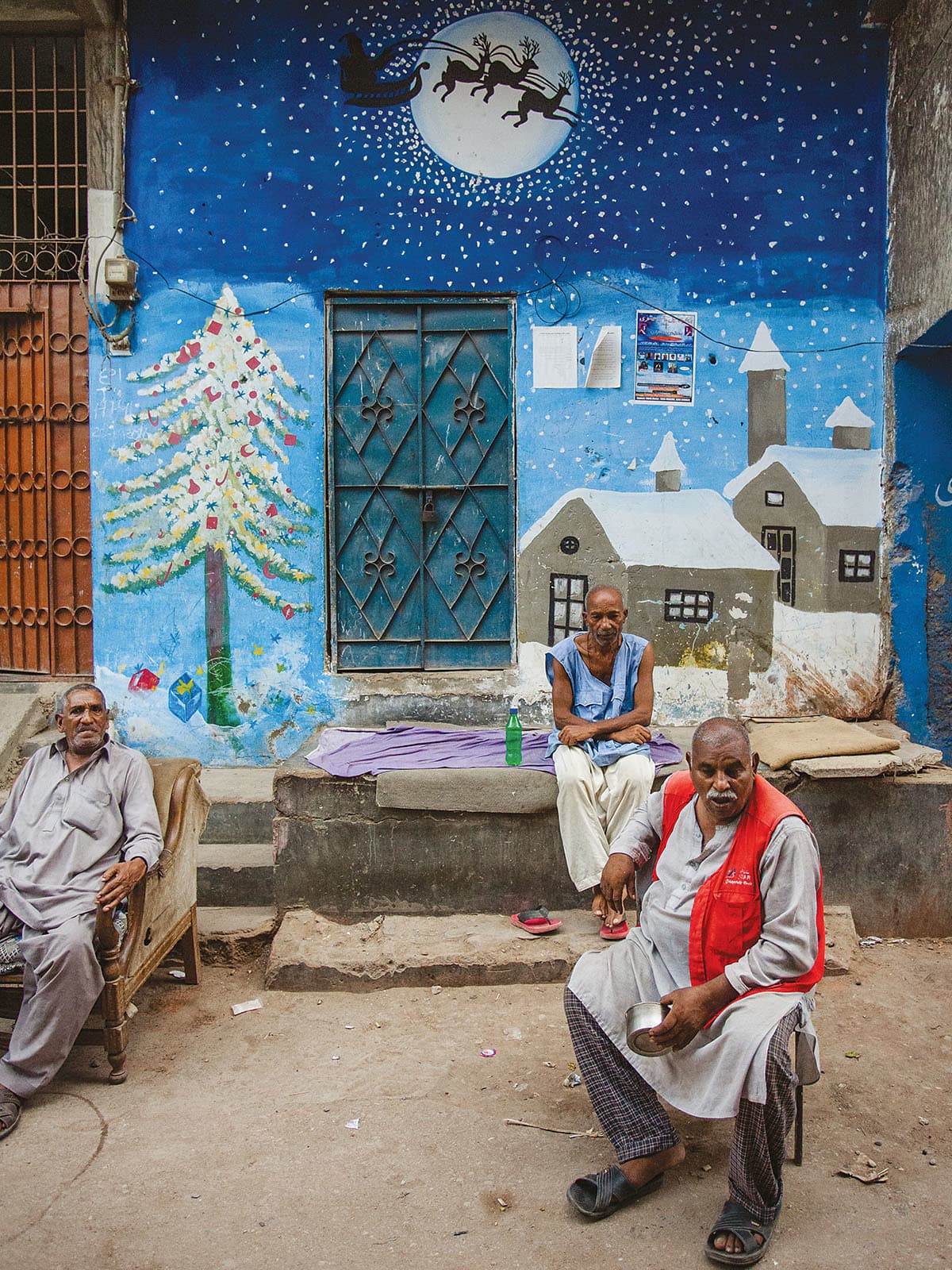Men sit in front of a Christmas mural painted on a wall in Essa Nagri, Karachi | Mohammad Ali, White Star Men sit in front of a Christmas mural painted on a wall in Essa Nagri, Karachi | Mohammad Ali, White Star