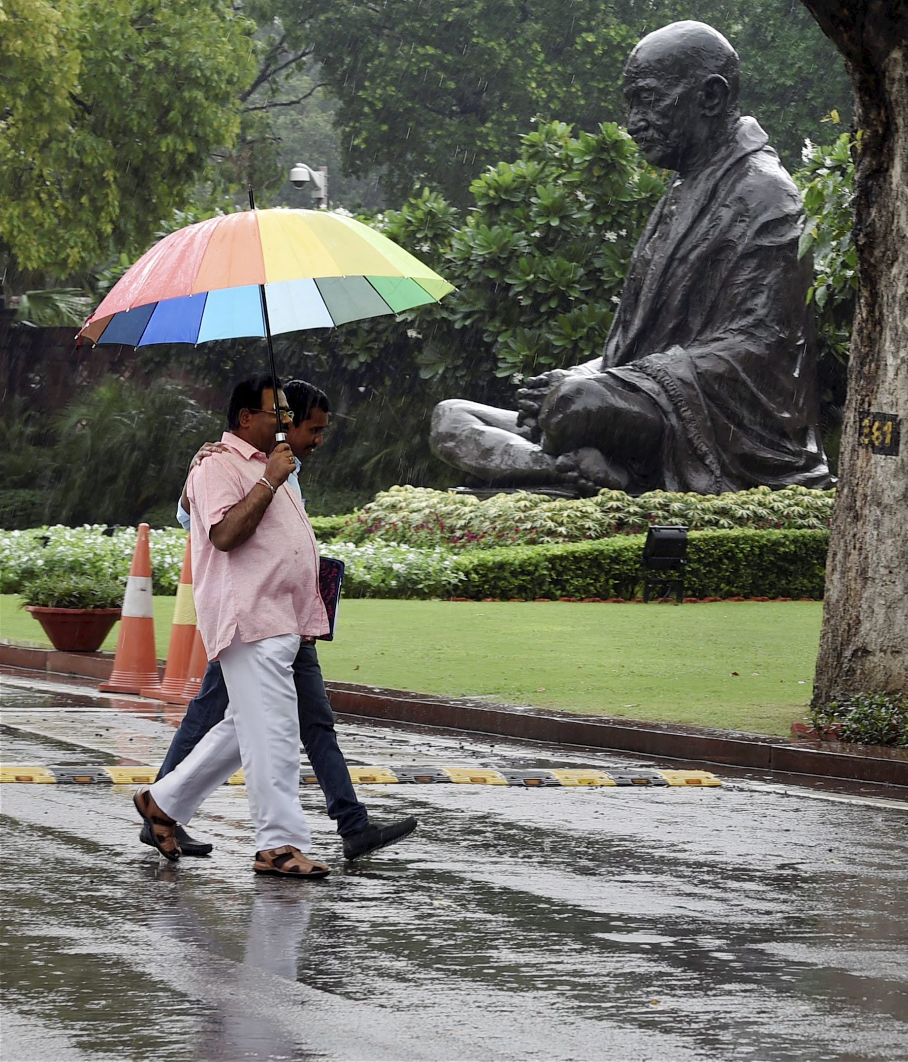 People take cover as they walk past the Mahatma Gandhi statue at the Parliament House. (Credit: PTI) People take cover as they walk past the Mahatma Gandhi statue at the Parliament House. (Credit: PTI)