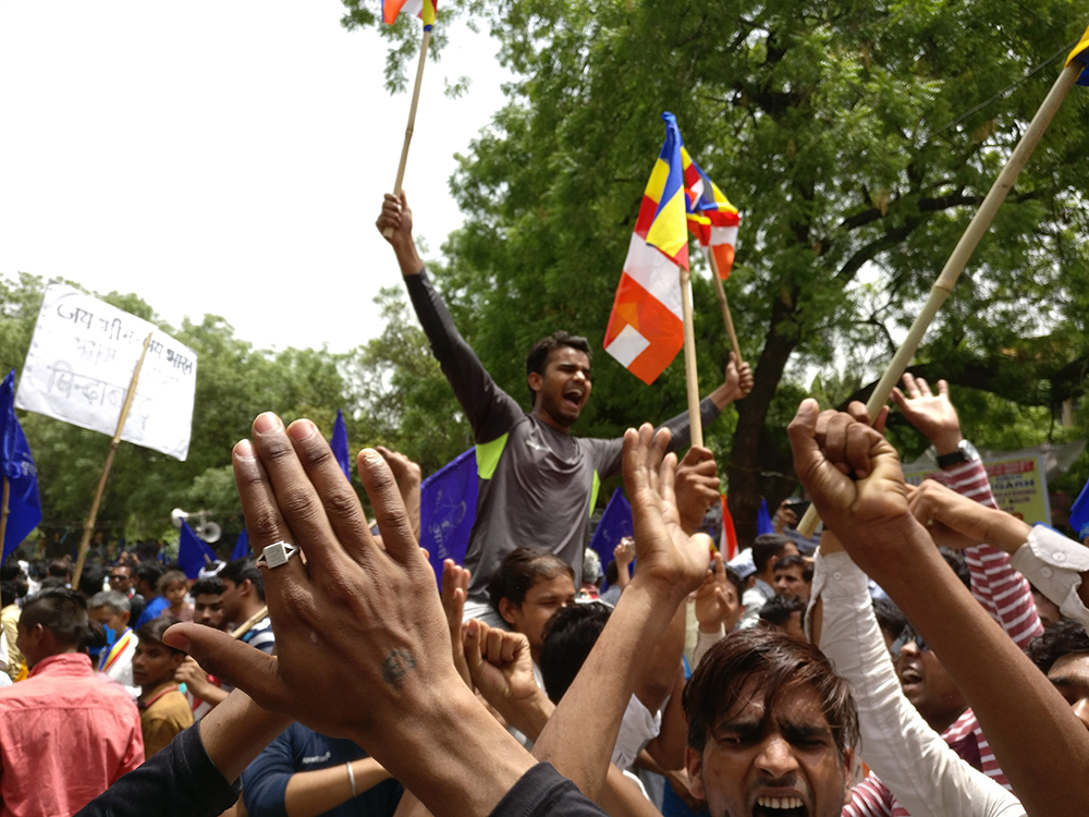 A man perched on someone's shoulders holds up two Buddhist flags | Photo credit: Shoaib Daniyal A man perched on someone's shoulders holds up two Buddhist flags | Photo credit: Shoaib Daniyal