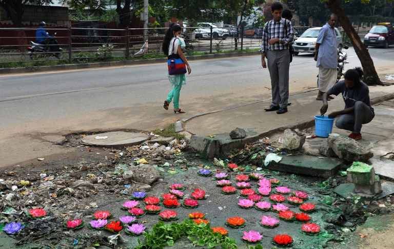 Baadal Nanjundaswamy pours paint around his art installation after placing artificial lotus flowers over a pothole filled with sewage at a pedestrian junction on Old Airport Road in Bengaluru on August 20, 2015. (Credit: Manjunath Kiran/AFP) Baadal Nanjundaswamy pours paint around his art installation after placing artificial lotus flowers over a pothole filled with sewage at a pedestrian junction on Old Airport Road in Bengaluru on August 20, 2015. (Credit: Manjunath Kiran/AFP)