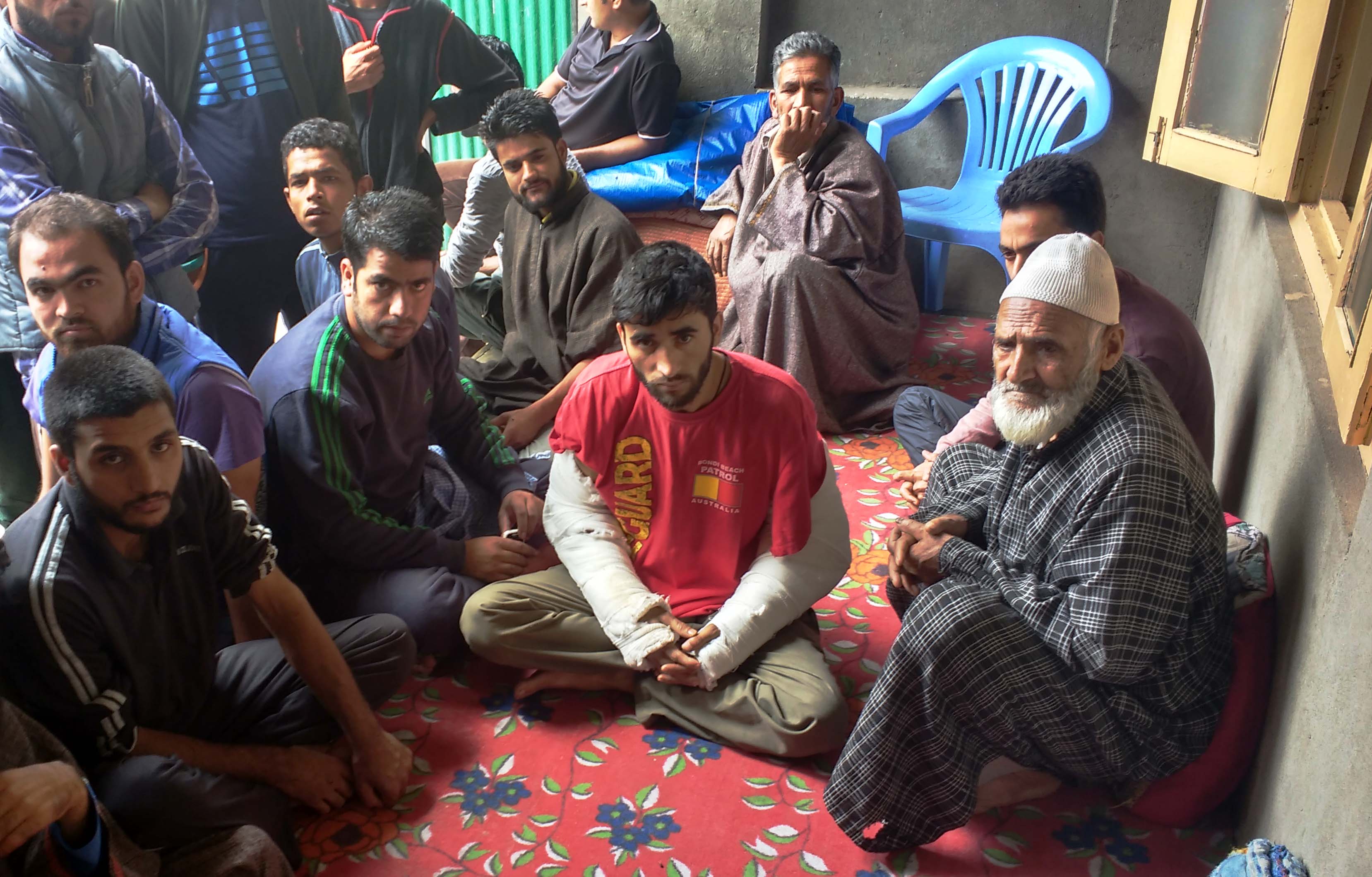 Zahoor Ahmad Mangoo (centre) sits on his front porch, still recovering from injuries. On the right, Mohammad Jabbar, visiting from Hadpora mohalla. (Photo credit: Rayan Naqash). Zahoor Ahmad Mangoo (centre) sits on his front porch, still recovering from injuries. On the right, Mohammad Jabbar, visiting from Hadpora mohalla. (Photo credit: Rayan Naqash).